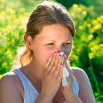 Teenager (girl) blowing her nose on a summer's day, green and yellow vegetation in the background