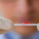 A drop of blood on top of a strip held between two hands, HEMATOLOGY